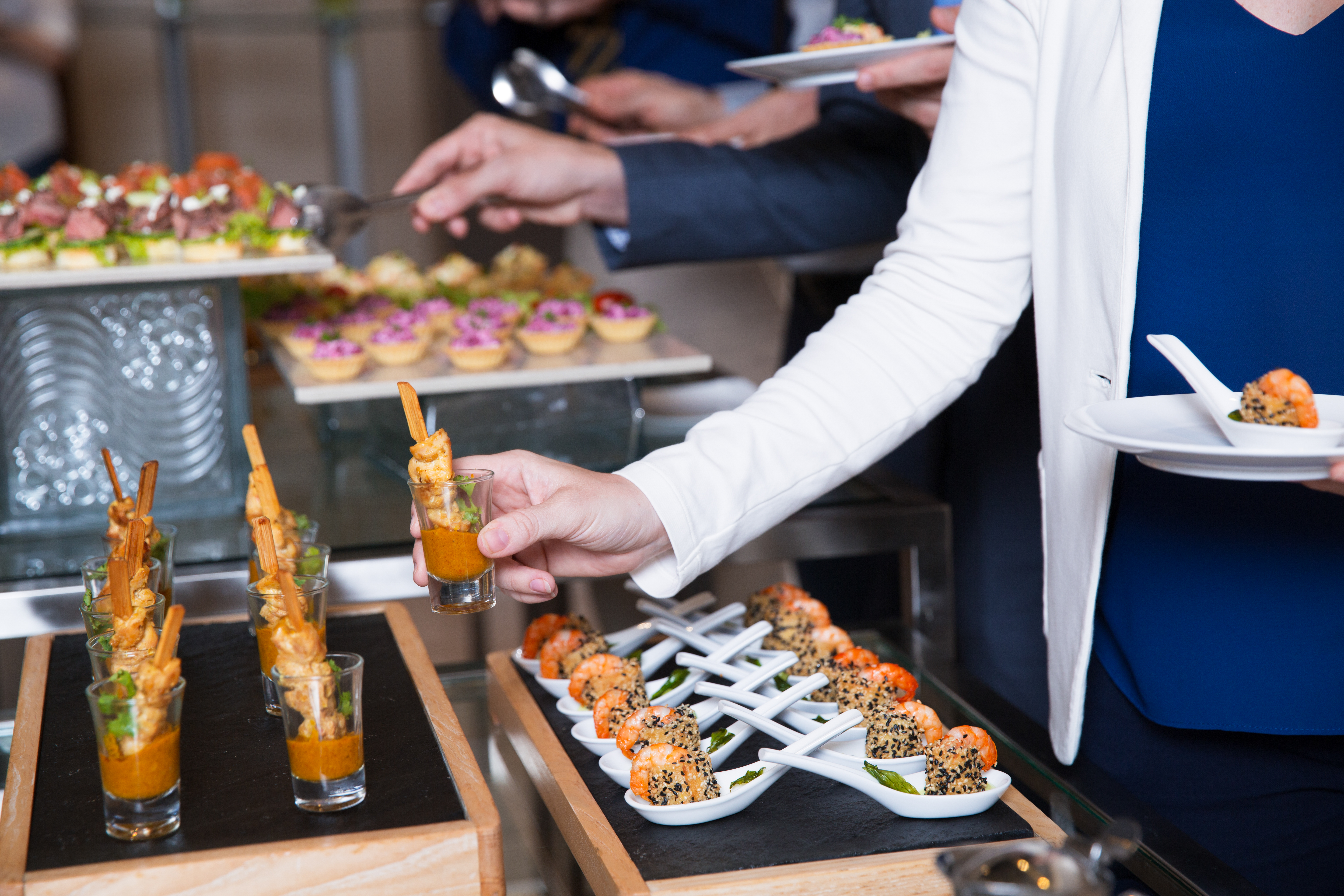 Cropped view of woman and blurred man in background taking snacks from buffet table